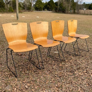 May include: Four wooden chairs with black metal frames, arranged in a row on a field of brown leaves.