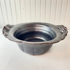 May include: A black ceramic bowl with two decorative handles on the sides. The bowl has a scalloped edge and a crackled glaze.