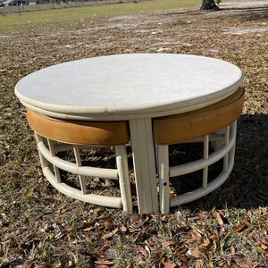 May include: A white round table with a white top and three brown cushioned seats. The table and seats are made of woven wicker.