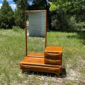 May include: A vintage wooden vanity with a mirror and three drawers. The vanity is made of a rich brown wood and has a mid-century modern design.
