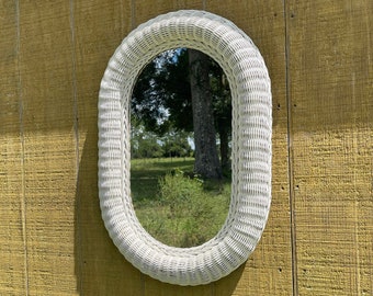 May include: White wicker oval mirror with a reflective surface. The mirror is hanging on a yellow wooden wall.