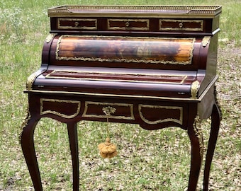 May include: A mahogany roll top desk with brass accents and a marquetry inlay. The desk has three drawers and a pull-out writing surface. The desk is on a set of cabriole legs.