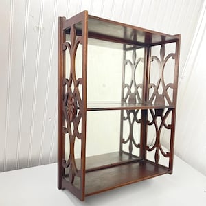 May include: A dark wood wall shelf with a mirror and two shelves. The shelf has a decorative, intricate design with a floral motif.