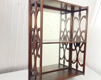 May include: A dark wood wall shelf with a mirror and two shelves. The shelf has a decorative, intricate design with a floral motif.