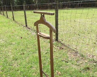 May include: A wooden valet stand with a top shelf, a hanger, and a lower shelf. The stand is brown and has a simple design.