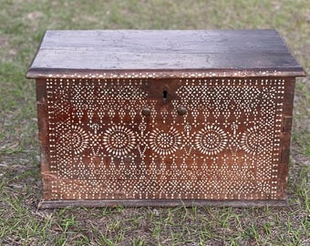 Puede incluir: Un cofre de madera vintage con intrincados diseños de incrustaciones blancas. El cofre tiene una tapa con bisagras y dos asas de latón.