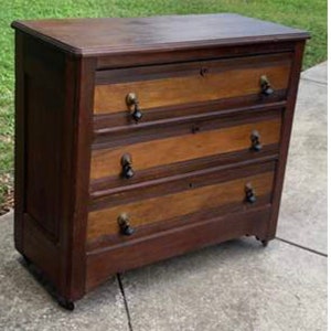 May include: A dark brown wooden dresser with four drawers. The drawers have a lighter wood veneer and black metal knobs. The dresser has a slightly distressed finish.