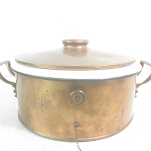 May include: A copper pot with a white enamel lining and a copper lid. The pot has two handles and a small knob on the lid.