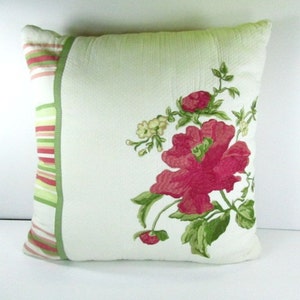 May include: A green and white pillow with a pink floral design. The pillow has a green and pink striped border.