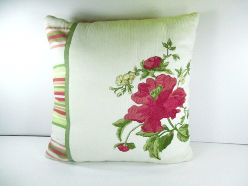 May include: A green and white pillow with a pink floral design. The pillow has a green and pink striped border.