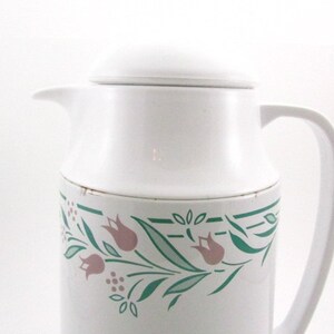 May include: White thermal carafe with a green and pink floral design. The carafe has a lid and a handle.