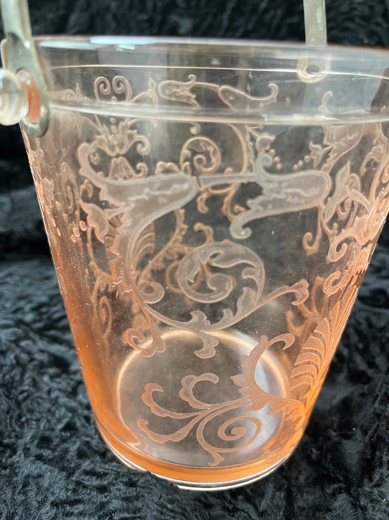 May include: A clear glass ice bucket with a silver handle. The bucket features a delicate etched floral design in a pale pink colour.