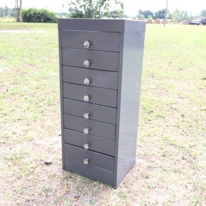 May include: A gray metal drawer cabinet with eight drawers and silver knobs. The cabinet is standing on a grassy surface.