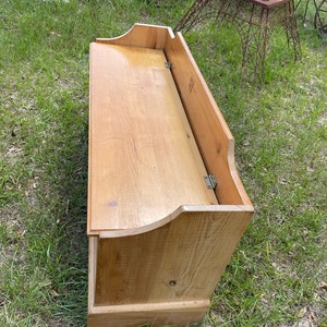 K&ouml;nnte beinhalten: Eine Holzaufbewahrungsbank mit einem Klappdeckel. Die Bank ist aus hellbraunem Holz gefertigt und hat ein schlichtes Design.