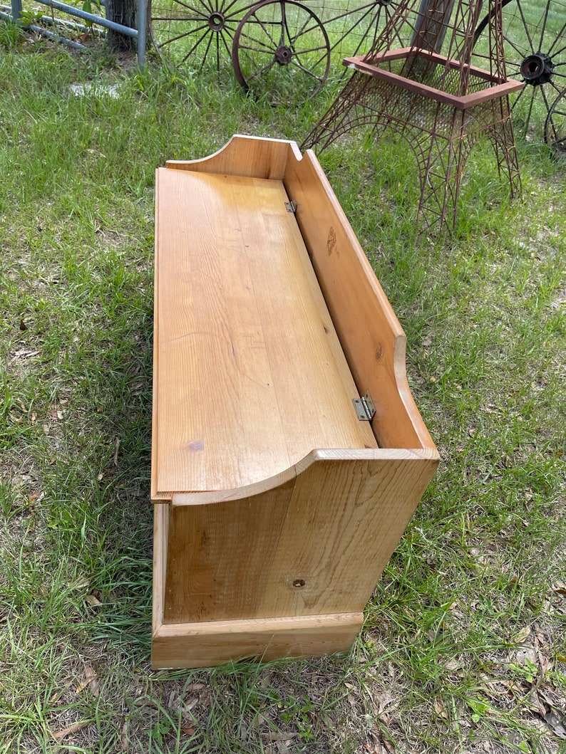 K&ouml;nnte beinhalten: Eine Holzaufbewahrungsbank mit einem Klappdeckel. Die Bank ist aus hellbraunem Holz gefertigt und hat ein schlichtes Design.