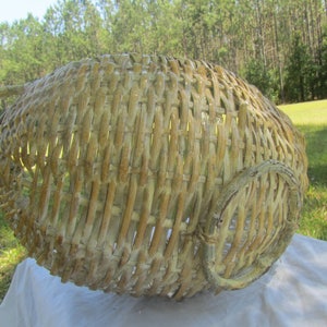 May include: A large, whitewashed wicker basket with a woven handle. The basket is made of natural materials and has a rustic, vintage look.