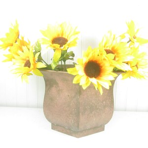 May include: A bouquet of yellow sunflowers in a brown, hexagonal planter.