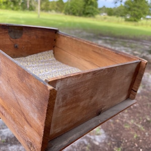 Puede incluir: Un caj&oacute;n de madera con un acabado marr&oacute;n claro y un forro estampado. El caj&oacute;n est&aacute; abierto y parece estar vac&iacute;o.
