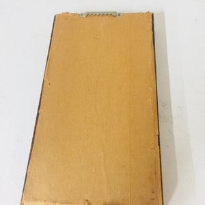 May include: A brown wooden picture frame with a brown paper backing. The frame has a sawtooth hanger on the back.
