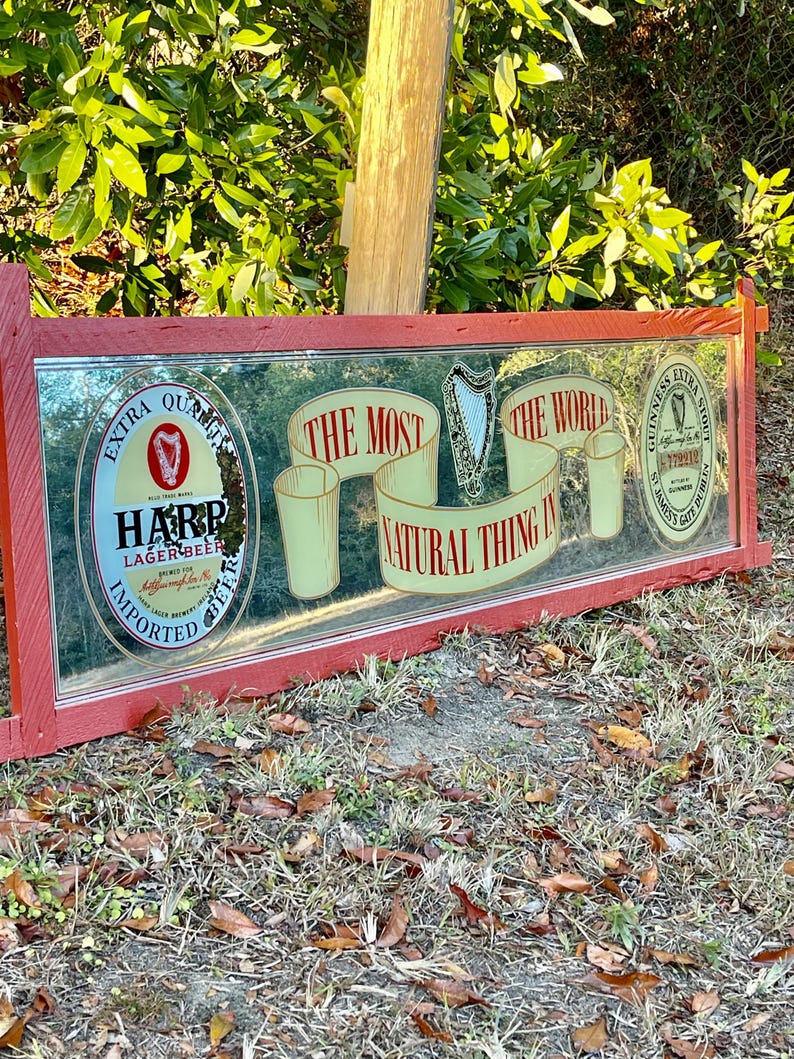 K&ouml;nnte beinhalten: Ein roter Spiegelrahmen mit einer Harp Lager Beer-Werbung. Die Anzeige zeigt eine Harfe, ein Glas Bier und den Text "Das nat&uuml;rlichste der Welt".