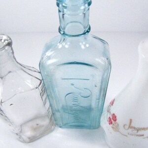 May include: Three glass bottles, one clear, one light blue, and one white with a floral design and the text "Jergens Lotion".