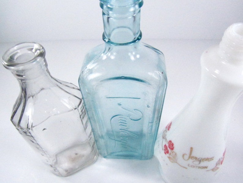 May include: Three glass bottles, one clear, one light blue, and one white with a floral design and the text "Jergens Lotion".