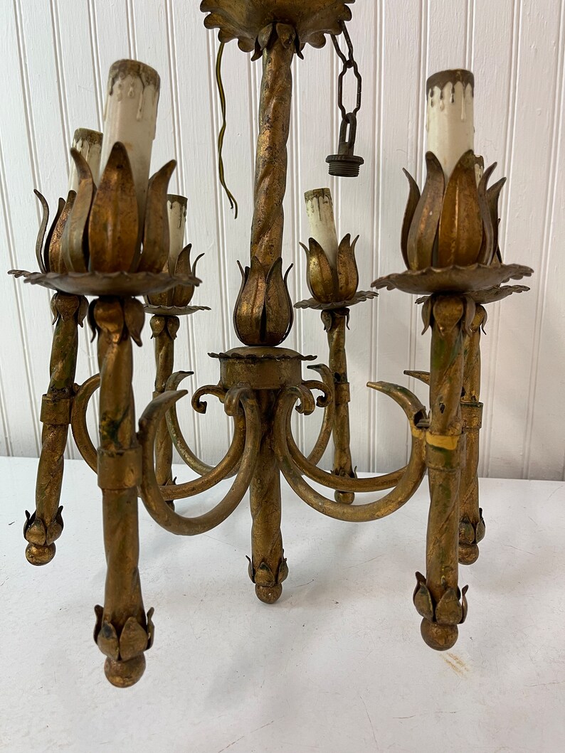 Pode incluir: Um candeeiro de teto de metal dourado com cinco luzes. O candeeiro de teto tem um design torcido e cada luz &eacute; cercada por uma decora&ccedil;&atilde;o em forma de flor.