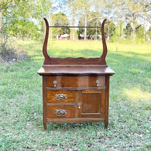May include: Antique wooden vanity with a beveled mirror, three drawers, and a cabinet door. The vanity has a dark wood finish and brass hardware.