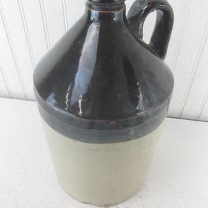 May include: A brown and cream glazed stoneware jug with a handle. The jug has a wide mouth and a rounded body.