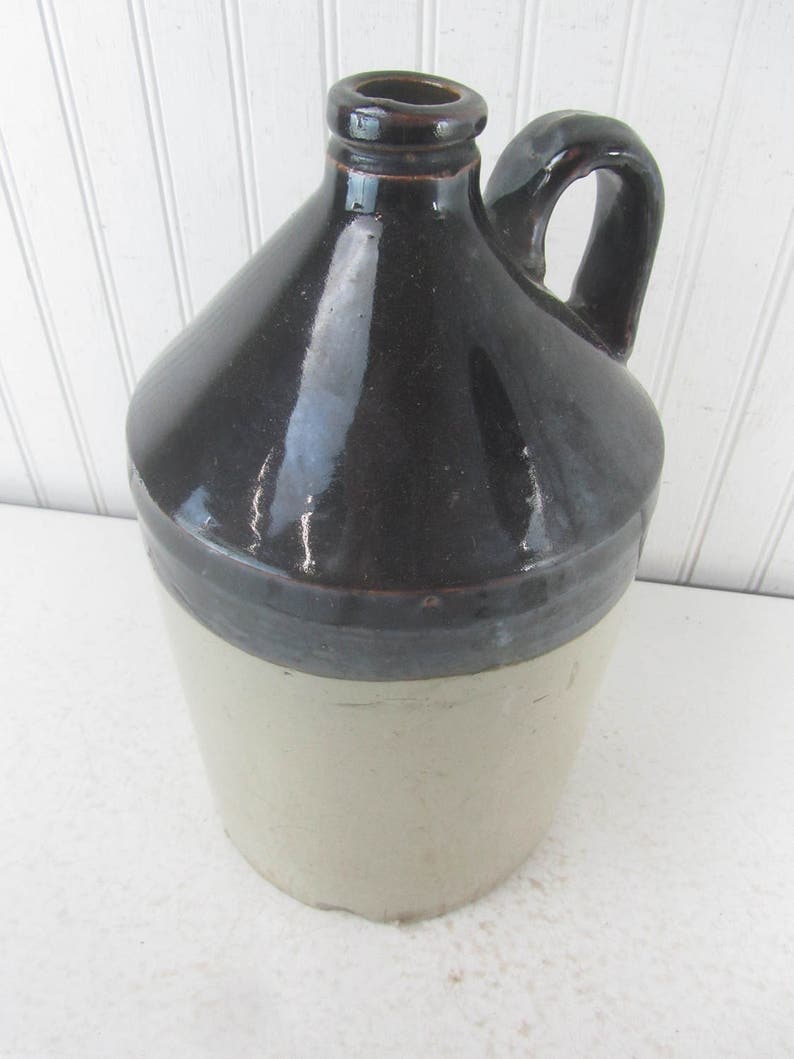 May include: A brown and cream glazed stoneware jug with a handle. The jug has a wide mouth and a rounded body.