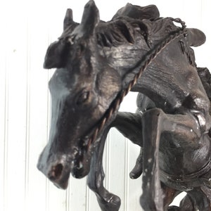 May include: A bronze sculpture of a horse rearing up on its hind legs, with a rope halter around its head. The horse is depicted in a dynamic pose, with its head thrown back and its front legs extended.