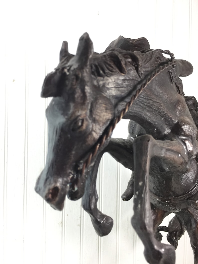 May include: A bronze sculpture of a horse rearing up on its hind legs, with a rope halter around its head. The horse is depicted in a dynamic pose, with its head thrown back and its front legs extended.