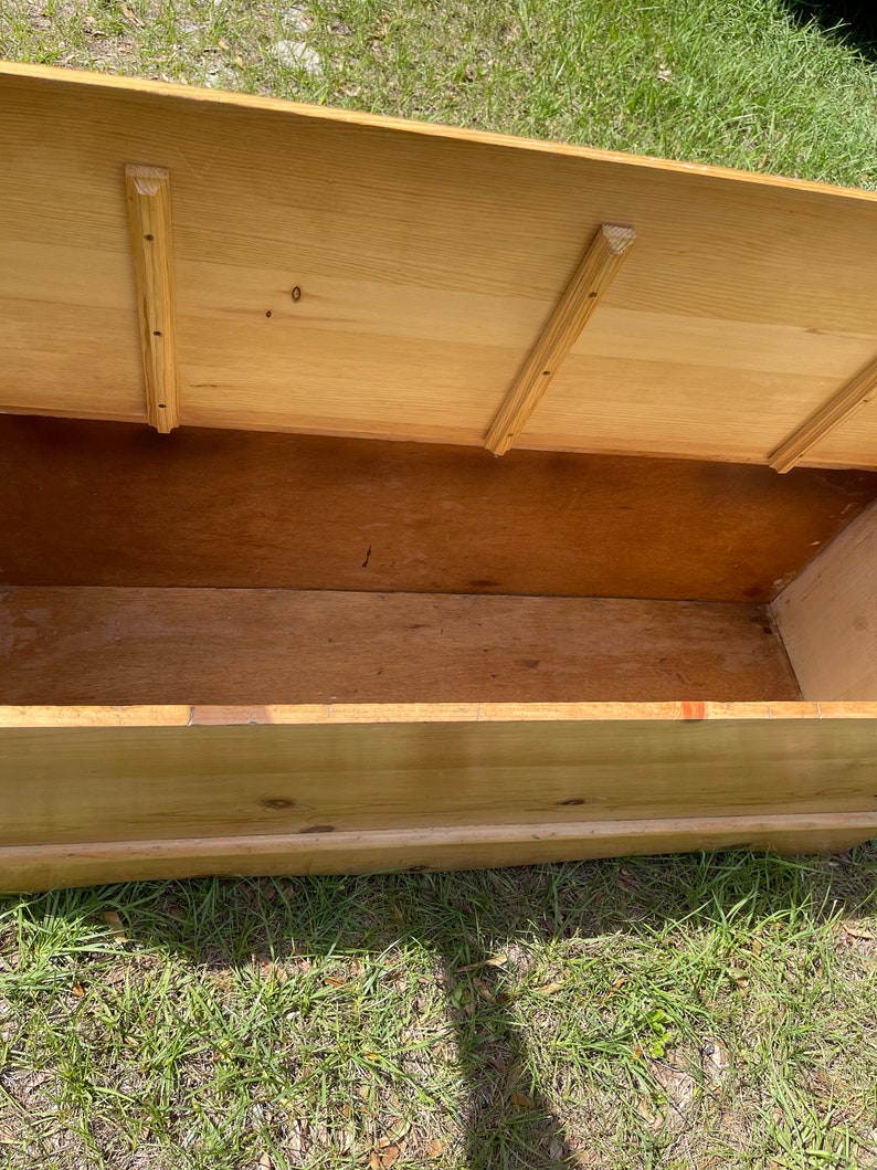 K&ouml;nnte beinhalten: Eine Holzkiste mit einem Scharnierdeckel, ge&ouml;ffnet, um den leeren Innenraum zu zeigen. Die Kiste ist aus hellem Holz gefertigt und hat ein schlichtes Design.