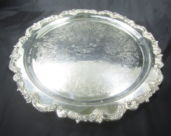 May include: A silver serving tray with an ornate, embossed design. The tray has a scalloped edge and features an inscription that reads "St. Louis Basketball Tournament - 1965".