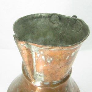 May include: A vintage copper pitcher with a worn, aged patina. The pitcher has a flared lip and a rounded base. The handle is missing.