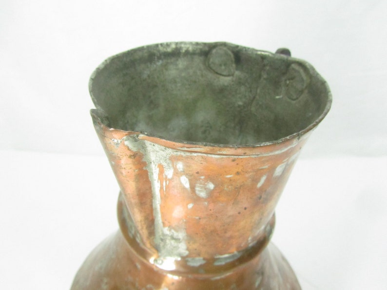 May include: A vintage copper pitcher with a worn, aged patina. The pitcher has a flared lip and a rounded base. The handle is missing.