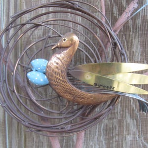 K&ouml;nnte beinhalten: Eine Metallskulptur eines Vogels in einem Nest mit blauen und wei&szlig;en Eiern. Der Vogel ist aus Kupfer und hat goldene Fl&uuml;gel. Die Skulptur ist signiert mit "Guenivere 87".