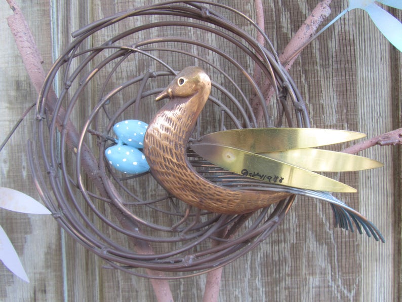 K&ouml;nnte beinhalten: Eine Metallskulptur eines Vogels in einem Nest mit blauen und wei&szlig;en Eiern. Der Vogel ist aus Kupfer und hat goldene Fl&uuml;gel. Die Skulptur ist signiert mit "Guenivere 87".
