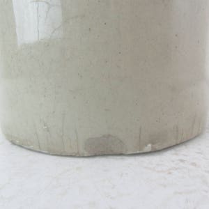 May include: A large, white ceramic crock with a slightly textured surface. The crock has a wide mouth and a rounded bottom. It shows signs of wear and tear, with some scratches and chips.