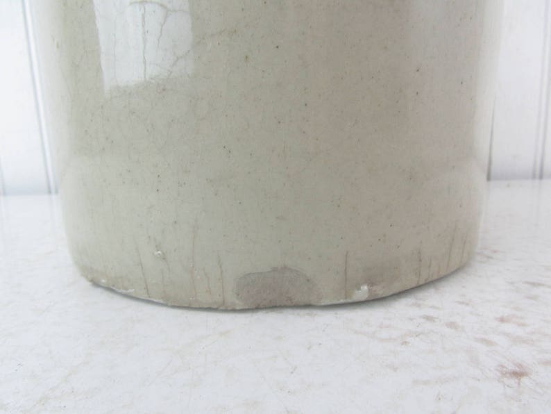 May include: A large, white ceramic crock with a slightly textured surface. The crock has a wide mouth and a rounded bottom. It shows signs of wear and tear, with some scratches and chips.