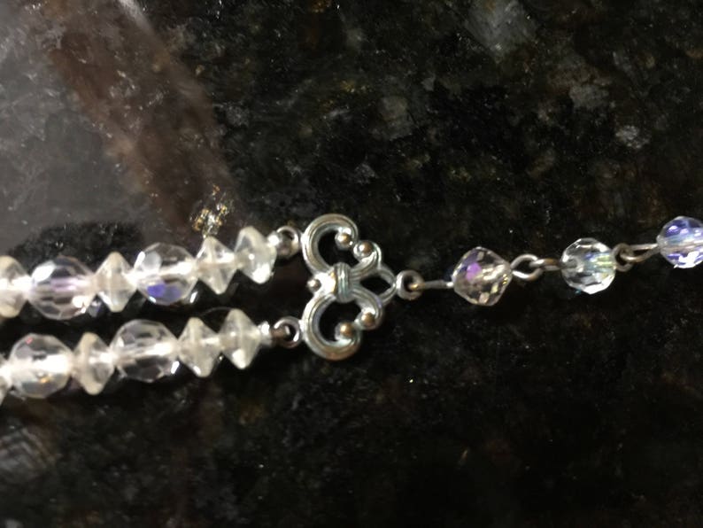 May include: A silver and crystal necklace with a decorative clasp. The necklace is made of two strands of clear crystal beads.