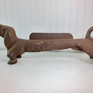 May include: A cast iron dachshund fire dog, a decorative fireplace accessory. The dog is brown and has a curled tail.