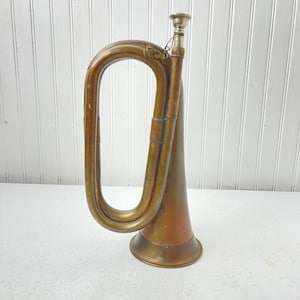 May include: A vintage brass bugle with a copper bell. The bugle has a long, curved mouthpiece and a silver-colored mouthpiece.