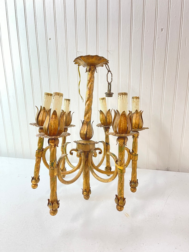 Pode incluir: Um candeeiro de teto de metal dourado com seis luzes. O candeeiro de teto tem um design de metal torcido e cada luz &eacute; cercada por uma pe&ccedil;a de metal em forma de flor.