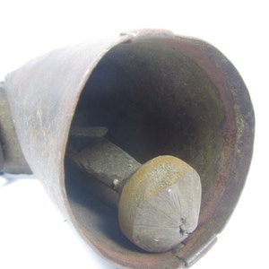 May include: A vintage cowbell with a leather strap and a wooden clapper. The bell is made of metal and has a rustic, aged appearance.