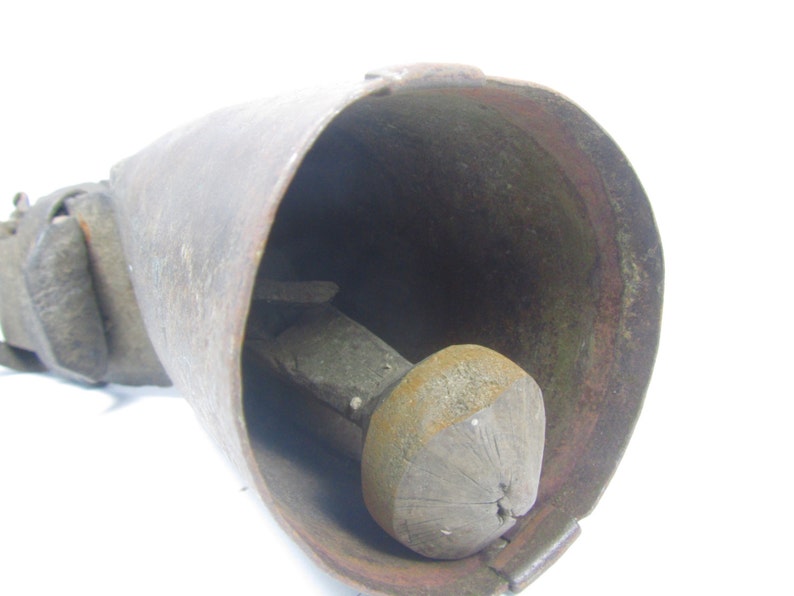 May include: A vintage cowbell with a leather strap and a wooden clapper. The bell is made of metal and has a rustic, aged appearance.