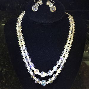 May include: A two-strand crystal necklace with a matching pair of clip-on earrings. The necklace features faceted crystal beads and the earrings have a teardrop shape.