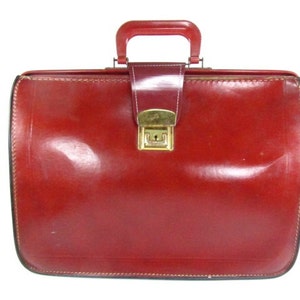 May include: A vintage red leather briefcase with a gold metal latch and a handle.
