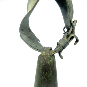 May include: A vintage cowbell with a worn leather strap. The bell is green and has a patina finish. The strap is brown and has a buckle.