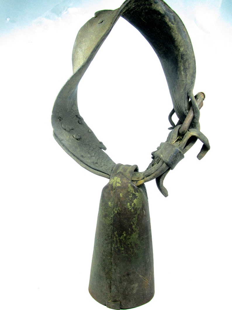 May include: A vintage cowbell with a worn leather strap. The bell is green and has a patina finish. The strap is brown and has a buckle.